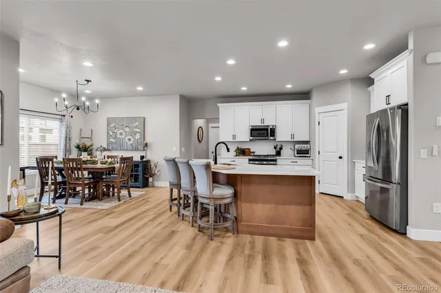 a kitchen with stainless steel appliances kitchen island granite countertop a refrigerator a stove a sink a dining table and chairs with wooden floor