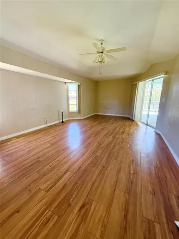 an empty room with wooden floor ceiling fan and windows