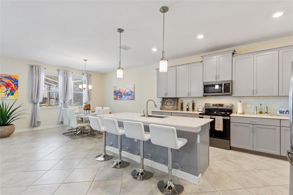 8811 Bally Neal Loop Davenport, FL 33896 - Photo 12 of 82 a kitchen with stainless steel appliances kitchen island granite countertop a stove a sink a dining table and chairs