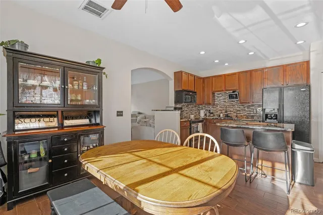 a kitchen with stainless steel appliances kitchen island granite countertop a stove a refrigerator a sink a dining table and chairs with wooden floor