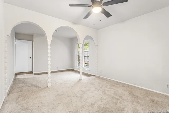an empty room with a chandelier fan and windows
