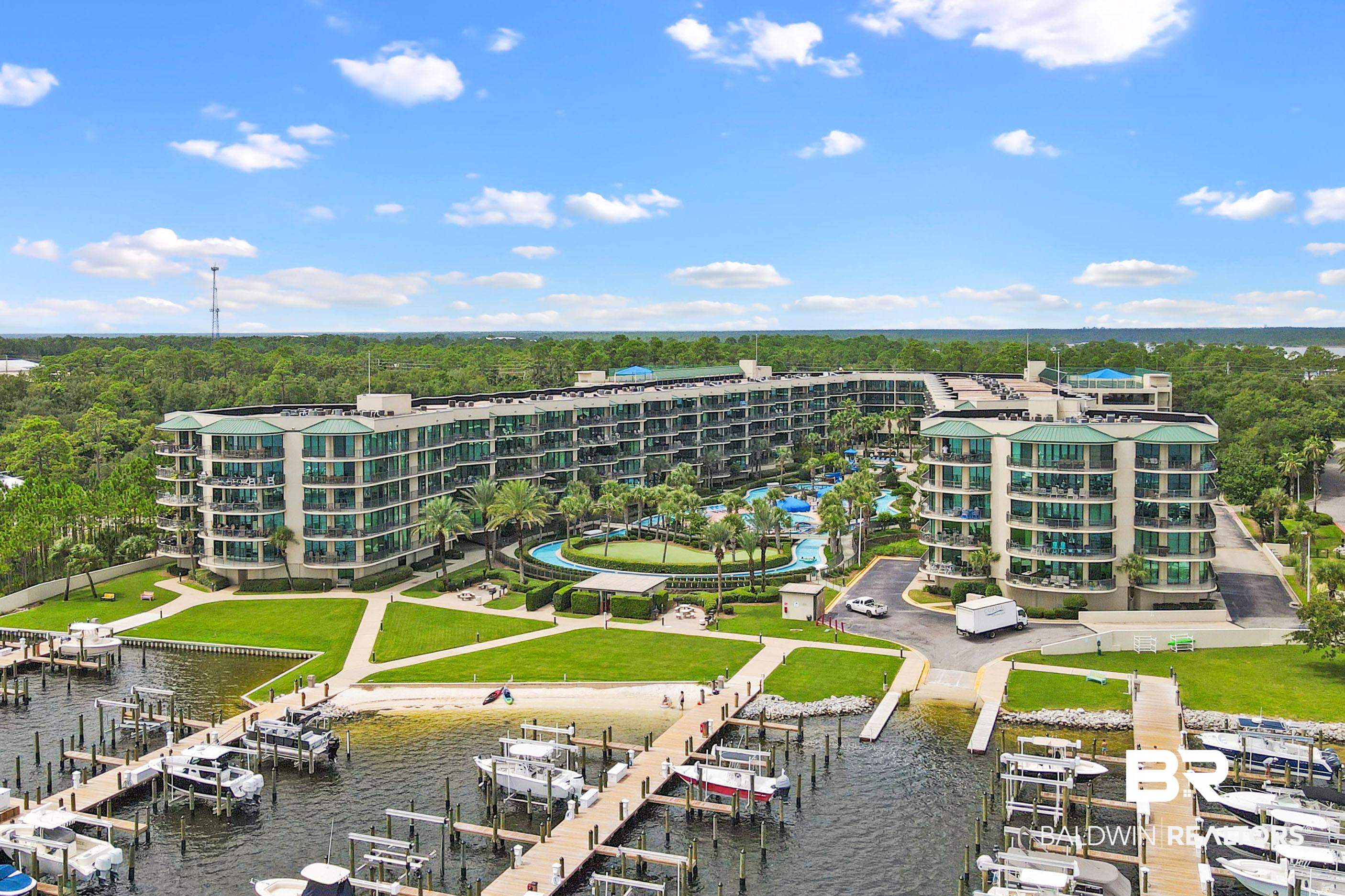 27580 Canal Road, Unit 1421 Orange Beach, AL 36561 - Photo 2 of 40 Expansive waterfront condominium complex featuring multiple residential buildings, a marina with numerous boat slips, a central pool area with landscaping, a putting green, and direct water access