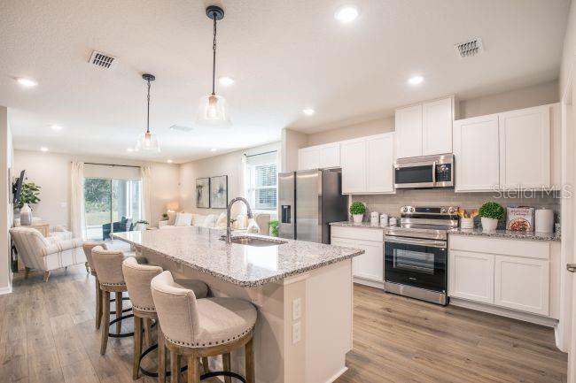 1407 Needle Palm Drive Edgewater, FL 32132 - Photo 5 of 28 a kitchen with stainless steel appliances kitchen island granite countertop a stove a sink a refrigerator a dining table and chairs with wooden floor
