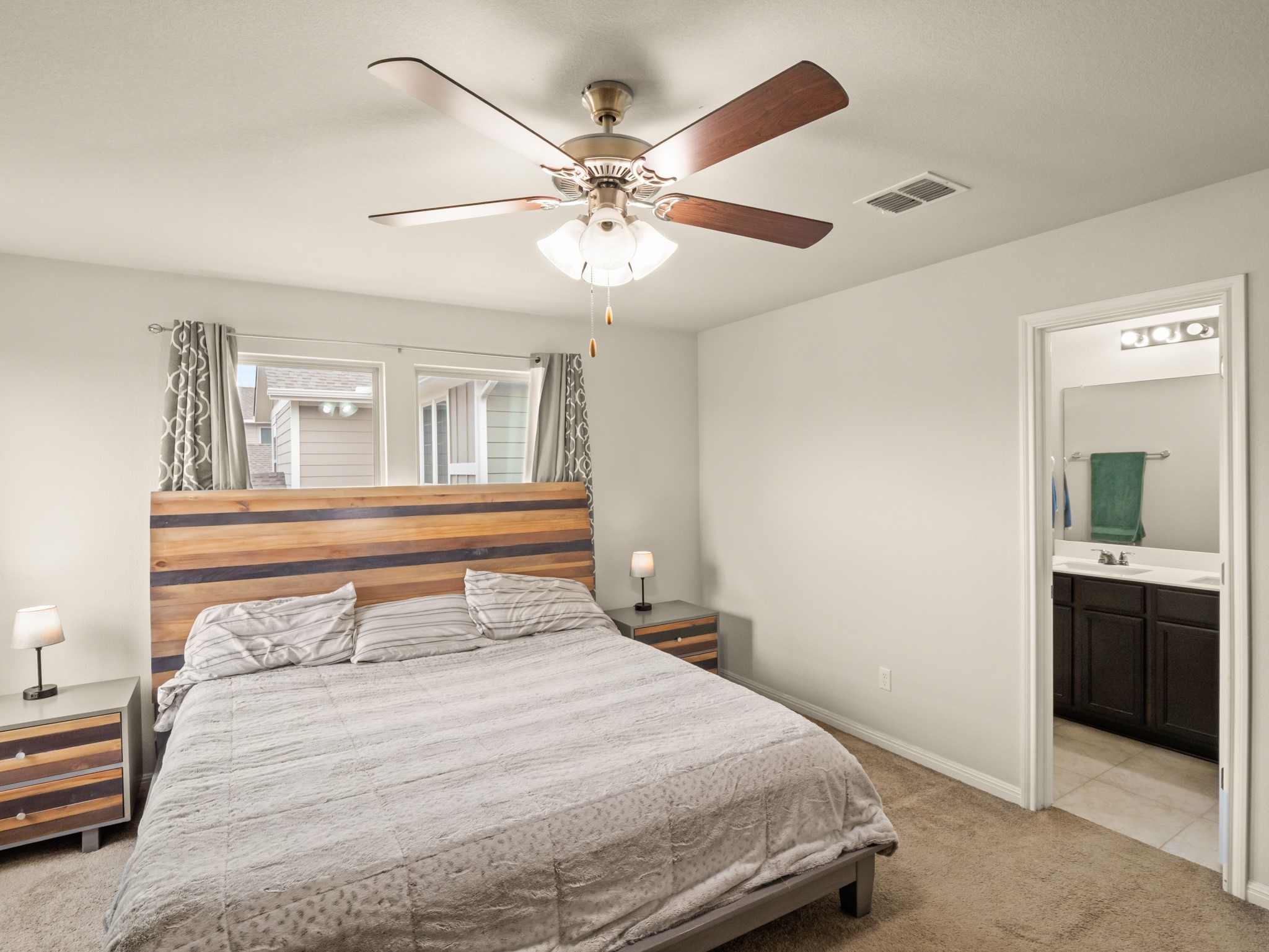 574 Nautical Loop Kyle, TX 78640 - Photo 18 of 23 A comfortable bedroom features a wooden headboard, two windows with drapes, and a ceiling fan for optimal airflow.