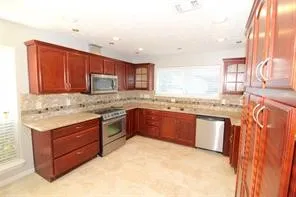 a kitchen with stainless steel appliances granite countertop wooden cabinets a stove a sink and a large window