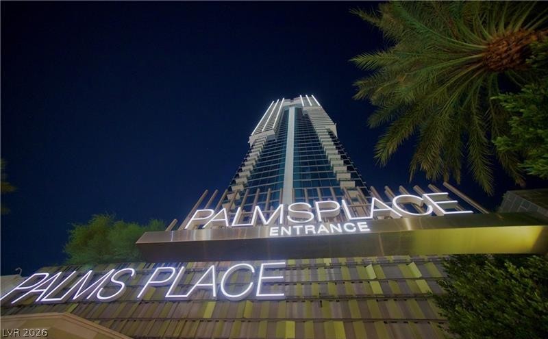 4381 West Flamingo Road, Unit 2819 Las Vegas, NV 89103 - Photo 8 of 9 A prominent entrance sign illuminates the pathway to a modern high-rise building at dusk.