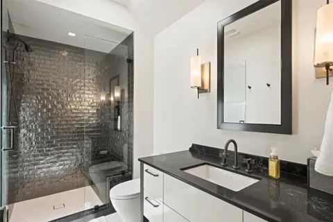 a bathroom with a granite countertop sink a toilet a mirror and shower
