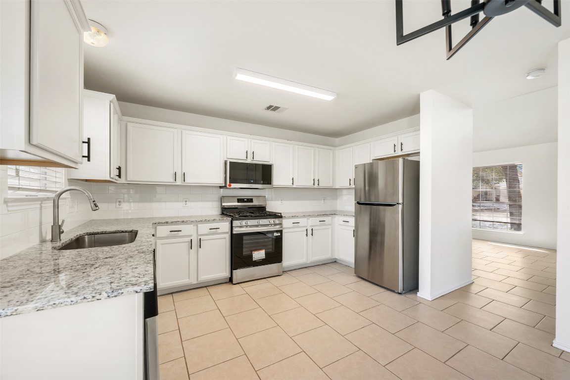 15216 Mandarin Crossing Pflugerville, TX 78660 - Photo 13 of 40 Kitchen featuring stainless steel appliances, white cabinets, light stone countertops, backsplash, and light tile patterned floors