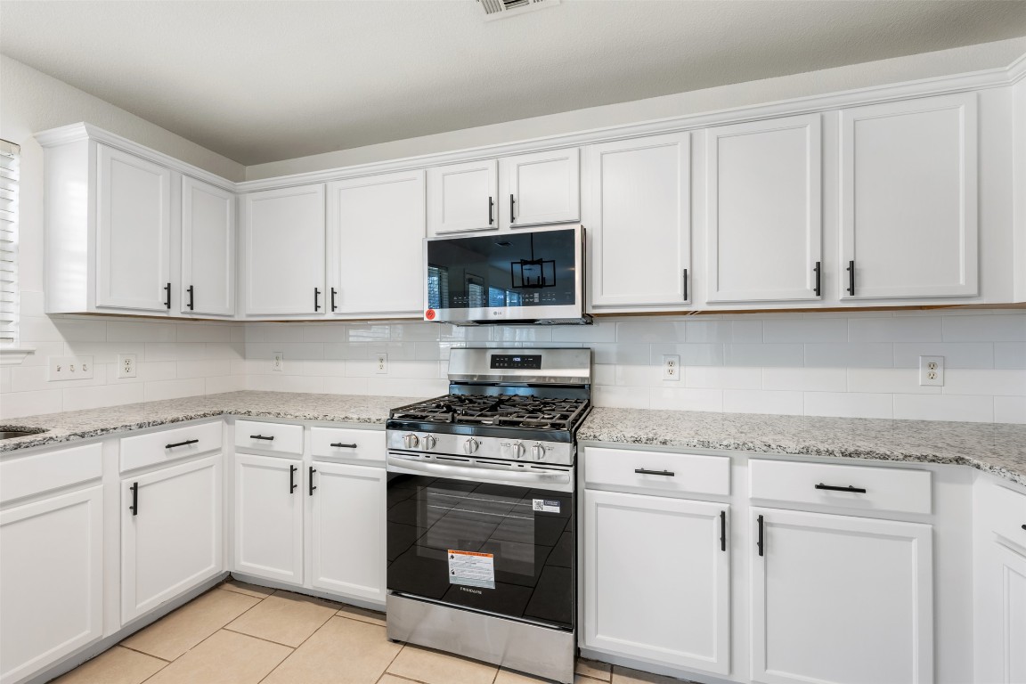 15216 Mandarin Crossing Pflugerville, TX 78660 - Photo 14 of 40 Kitchen featuring stainless steel appliances, light stone countertops, white cabinetry, and backsplash
