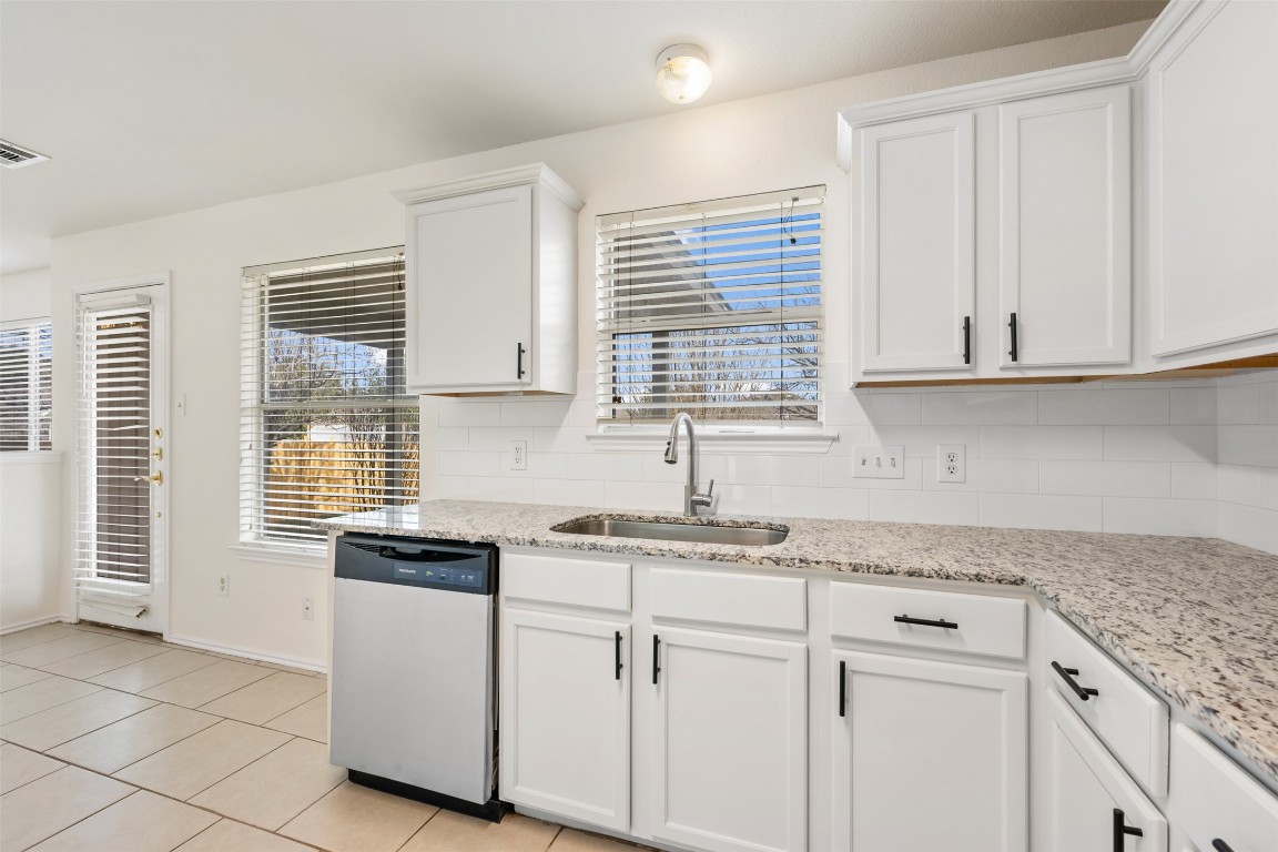 15216 Mandarin Crossing Pflugerville, TX 78660 - Photo 15 of 40 Kitchen featuring stainless steel dishwasher, white cabinetry, light stone countertops, and backsplash