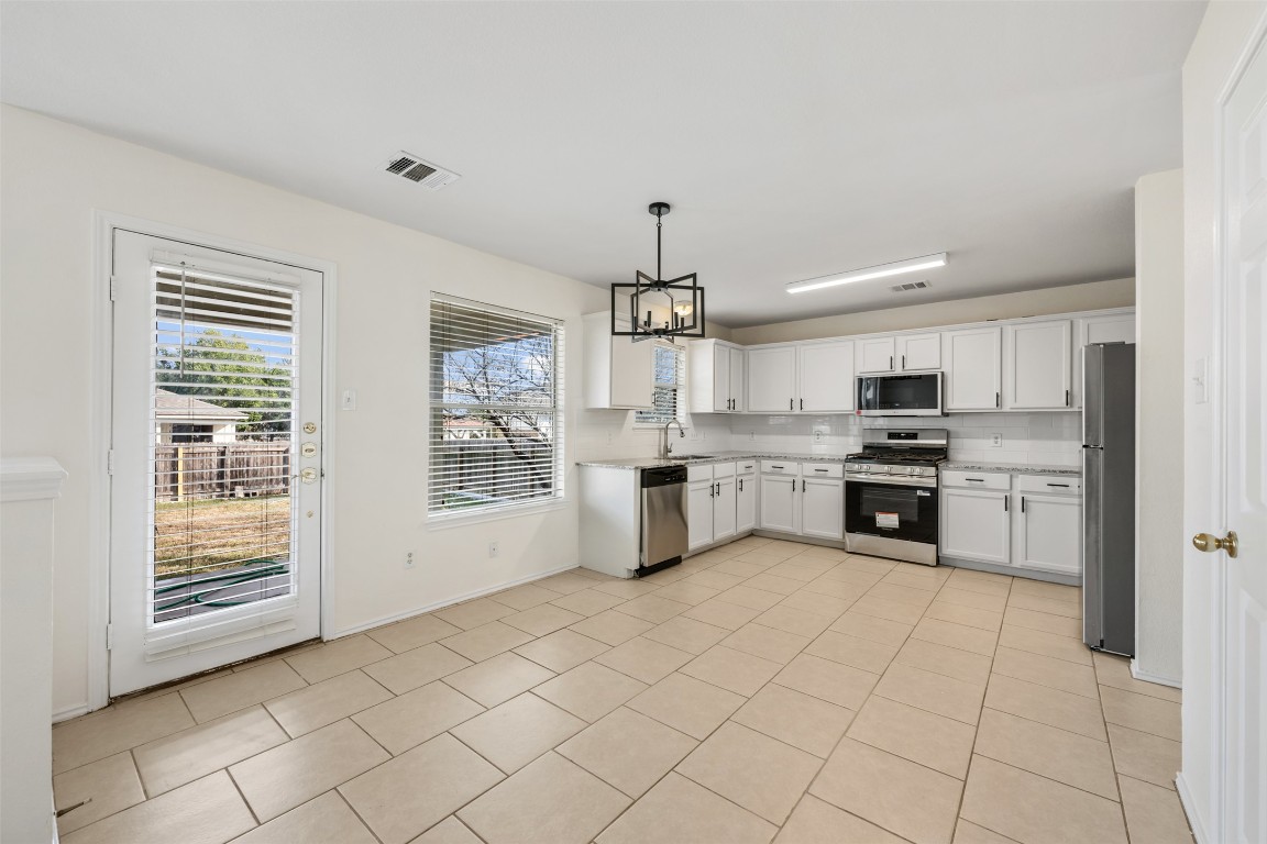 15216 Mandarin Crossing Pflugerville, TX 78660 - Photo 17 of 40 Kitchen featuring a chandelier, stainless steel appliances, white cabinetry, hanging light fixtures, and light tile patterned floors
