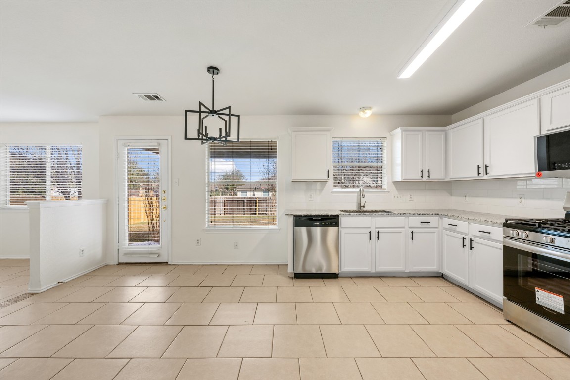 15216 Mandarin Crossing Pflugerville, TX 78660 - Photo 10 of 40 Kitchen featuring appliances with stainless steel finishes, decorative light fixtures, white cabinetry, a chandelier, and light tile patterned floors