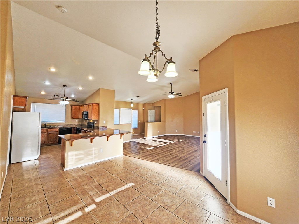3680 Ravine Avenue Pahrump, NV 89048 - Photo 6 of 28 Kitchen with ceiling fan with notable chandelier, brown cabinetry, black appliances, a kitchen bar, and a peninsula