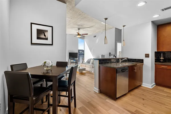 a kitchen with stainless steel appliances granite countertop a refrigerator a stove a sink a dining table and chairs with wooden floor