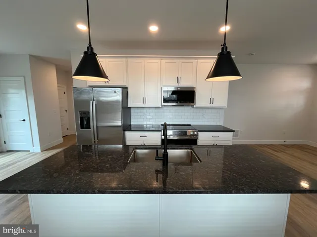 a kitchen with stainless steel appliances a sink a stove a refrigerator and white cabinets