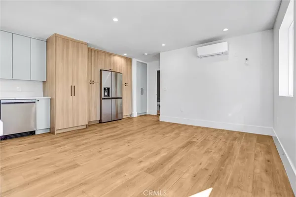 a view of an empty room with wooden floor and a kitchen