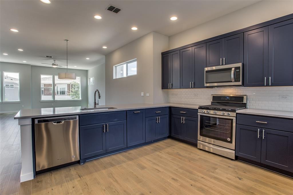 a kitchen with stainless steel appliances granite countertop wooden cabinets a stove a microwave and wooden floors