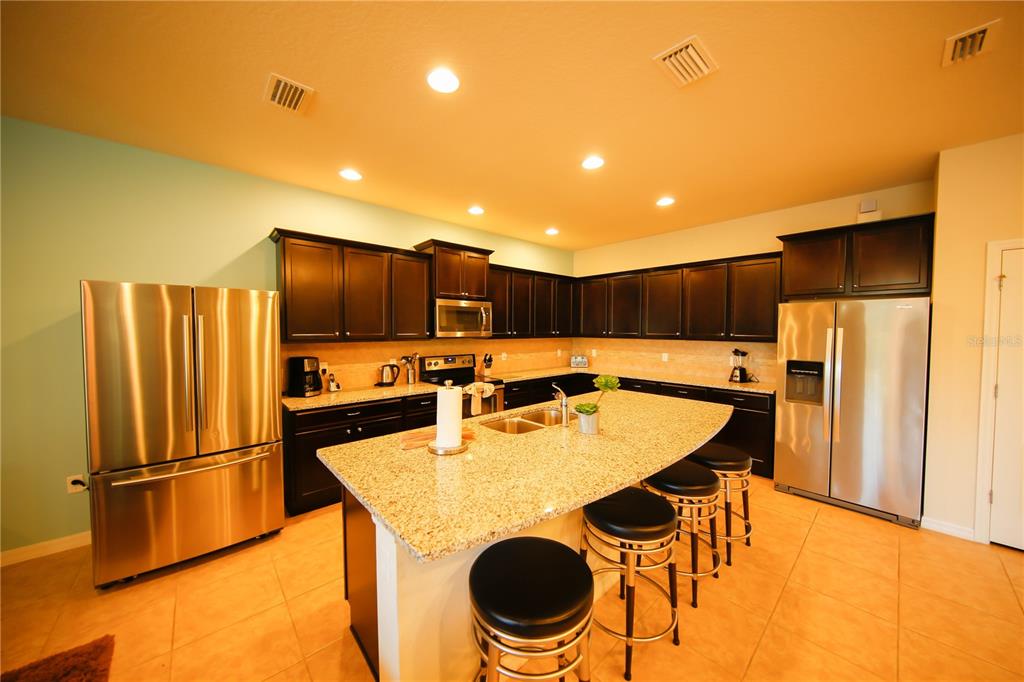 8809 Rhodes Street Kissimmee, FL 34747 - Photo 3 of 49 a kitchen with stainless steel appliances granite countertop a refrigerator a stove a sink dishwasher and a refrigerator with wooden floor