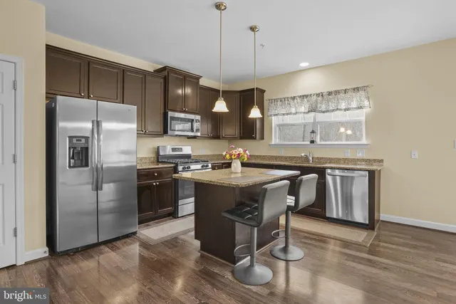 a kitchen with stainless steel appliances granite countertop a refrigerator a sink dishwasher a stove and a refrigerator with wooden floor