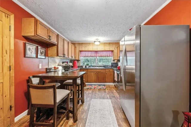 a kitchen with stainless steel appliances granite countertop a refrigerator a stove a sink a dining table and chairs with wooden floor