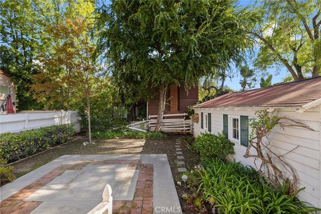 a view of a white house next to a yard with flower plants