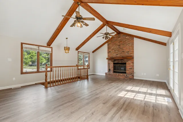 an empty room with wooden floor staircase and windows