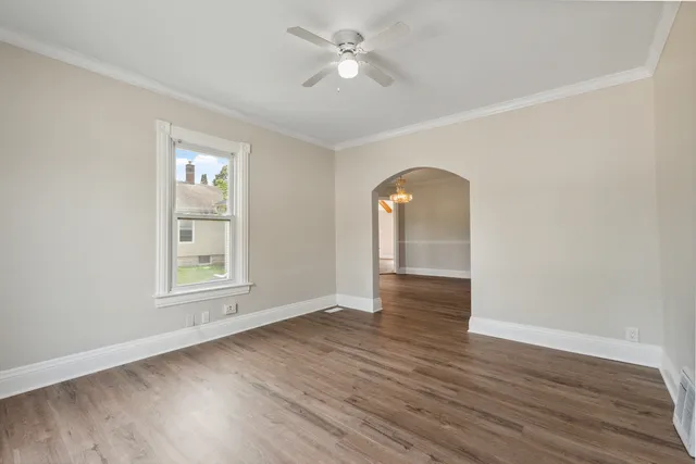 an empty room with wooden floor chandelier fan and windows