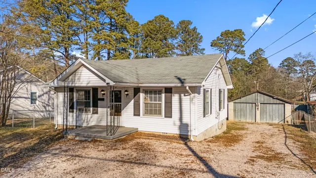 a view of a white house with a large tree and wooden fence