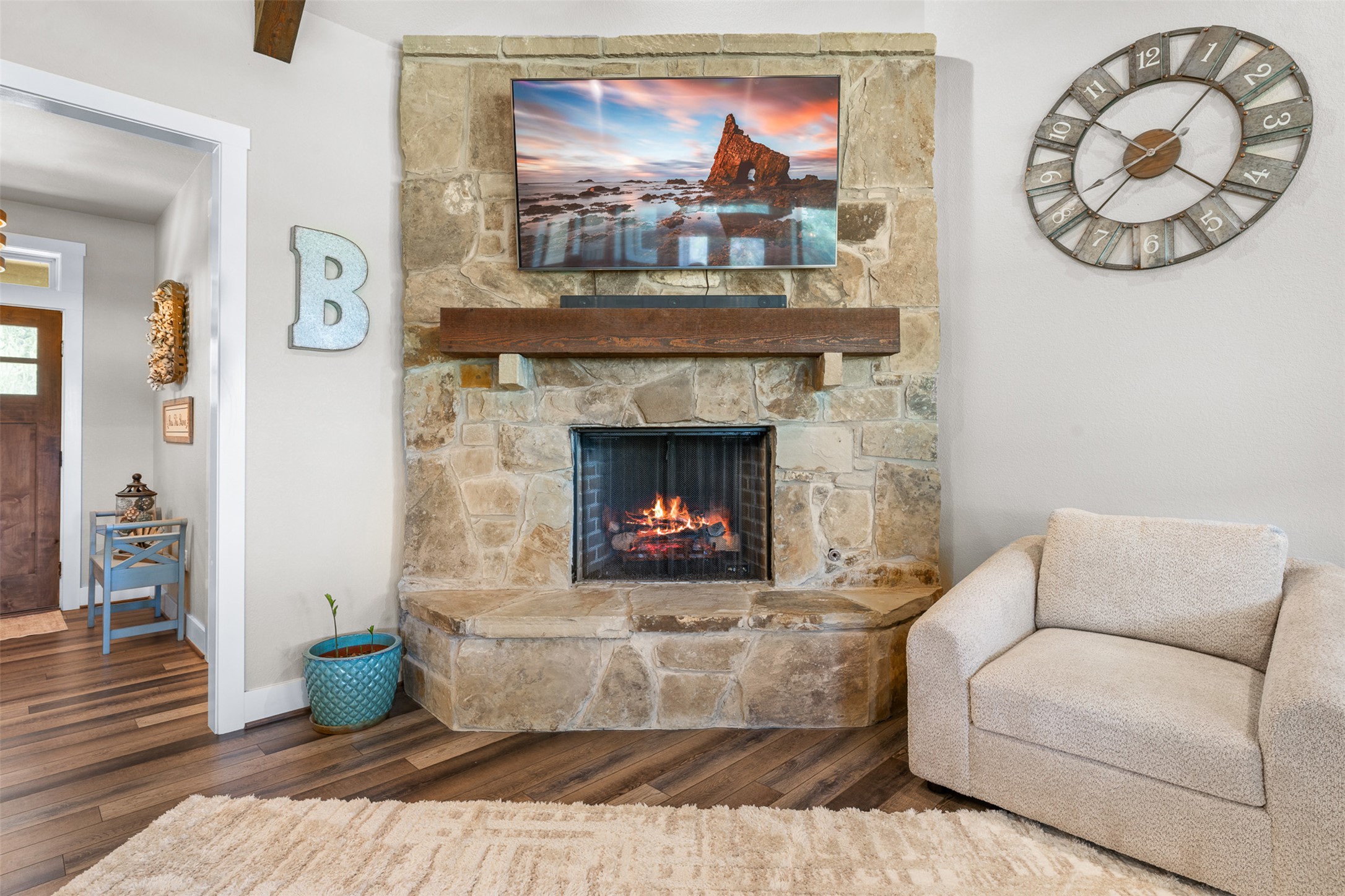 1306 22 Hills Road Gause, TX 77857 - Photo 33 of 40 Stone-clad fireplace featuring a wood-beam mantel and hearth, with wood-finish flooring extending into the doorway