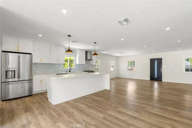 a kitchen with stainless steel appliances granite countertop a refrigerator a sink dishwasher and white cabinets with wooden floor