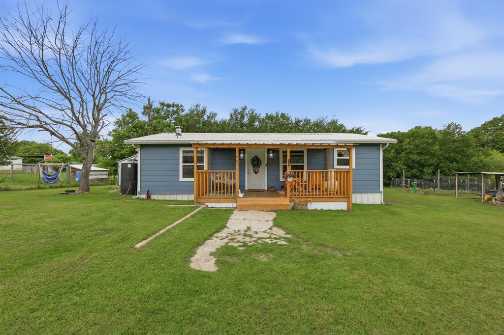The property features a blue exterior with a white roof, a wooden porch with railings, and a front door with a decorative glass insert