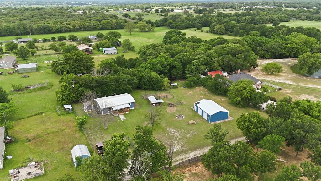 767 East Barry Street Azle, TX 76020 - Photo 12 of 40 This property features a main residence with a covered front porch, a separate blue and white outbuilding, and a variety of mature trees and green spaces