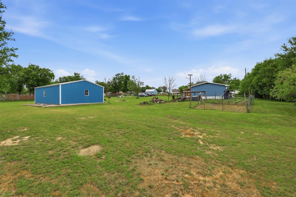 767 East Barry Street Azle, TX 76020 - Photo 14 of 40 The property includes an expansive grassy yard with a blue outbuilding featuring white trim and windows