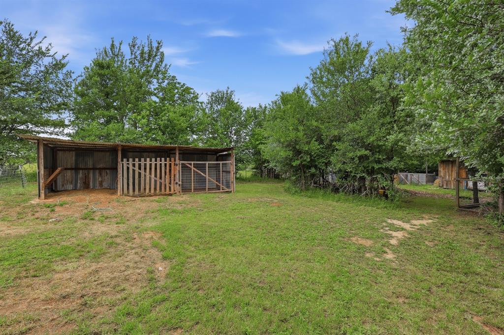 767 East Barry Street Azle, TX 76020 - Photo 15 of 40 The property includes a substantial grassy area with a wooden shelter featuring a corrugated metal roof and enclosed sections