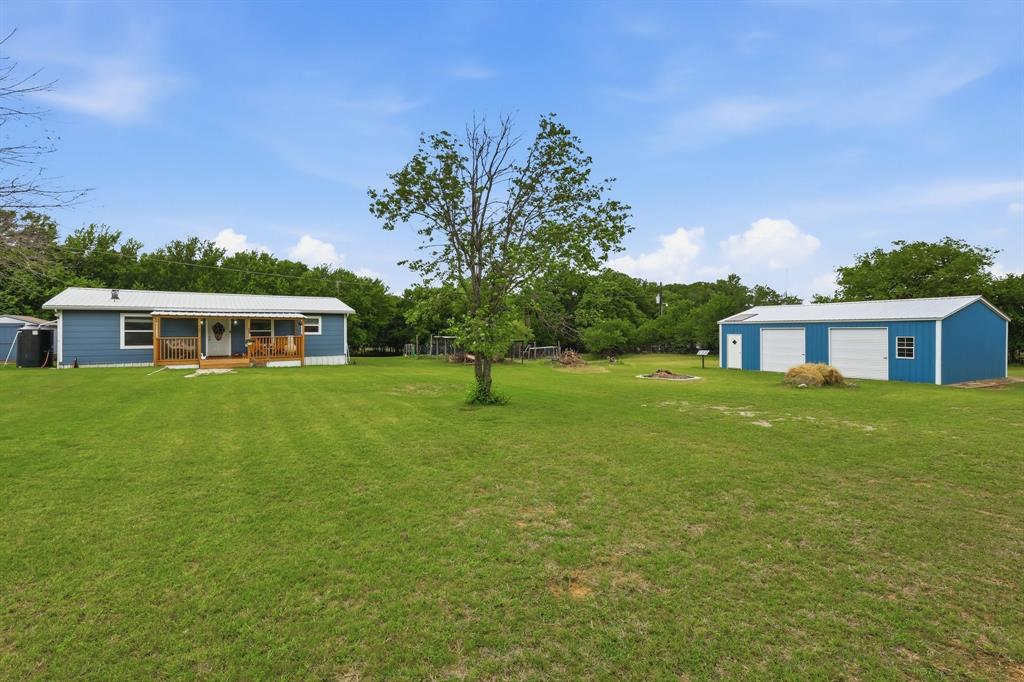 767 East Barry Street Azle, TX 76020 - Photo 17 of 40 The property features an extensive green lawn, a covered front porch with wooden railings, and a detached blue building with two garage doors and a white side door