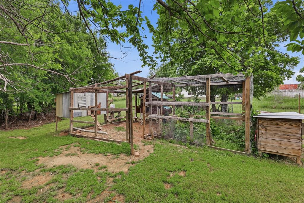 767 East Barry Street Azle, TX 76020 - Photo 18 of 40 The property includes a fenced enclosure with a wooden structure and a metal shed, set within a grassy area with mature trees