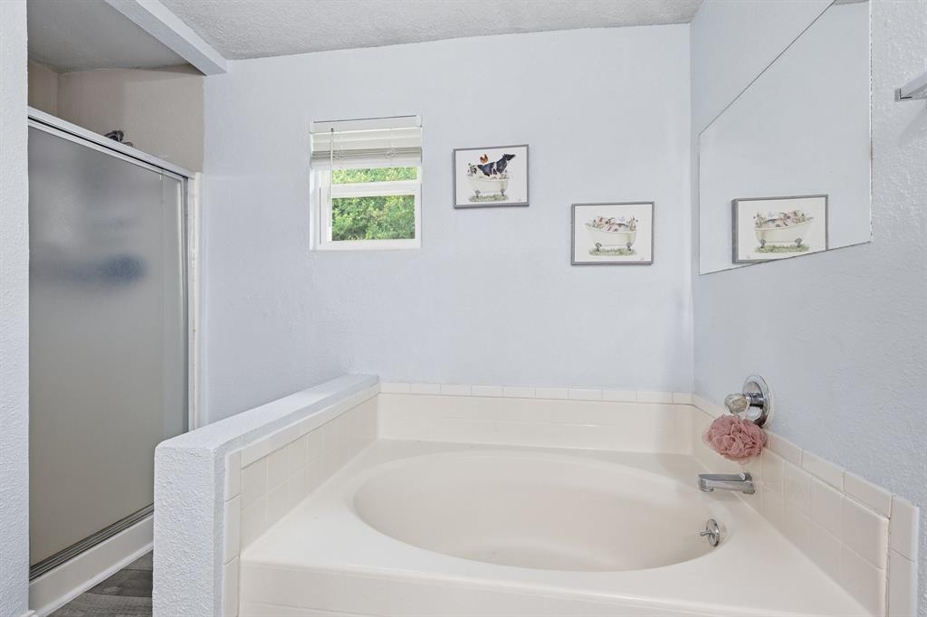 767 East Barry Street Azle, TX 76020 - Photo 27 of 40 Bathroom featuring a built-in bathtub, a window, and a shower with a frosted glass door