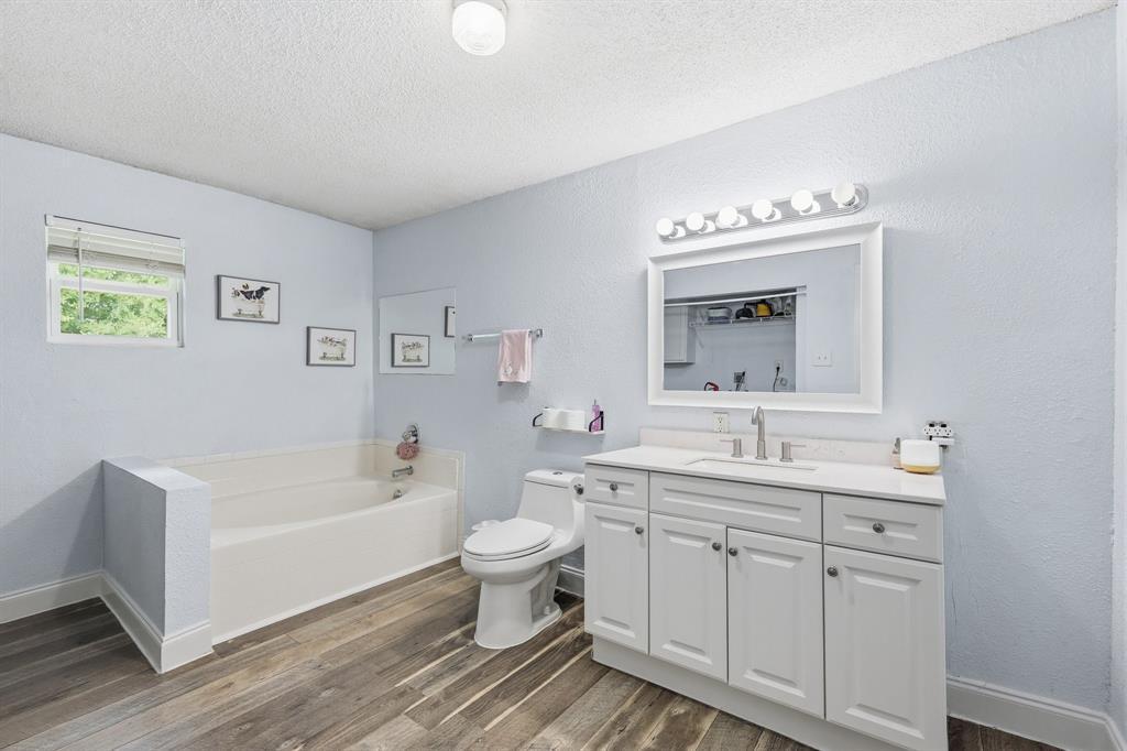 767 East Barry Street Azle, TX 76020 - Photo 29 of 40 The bathroom features a spacious bathtub, a vanity with a white countertop, and wood-look flooring