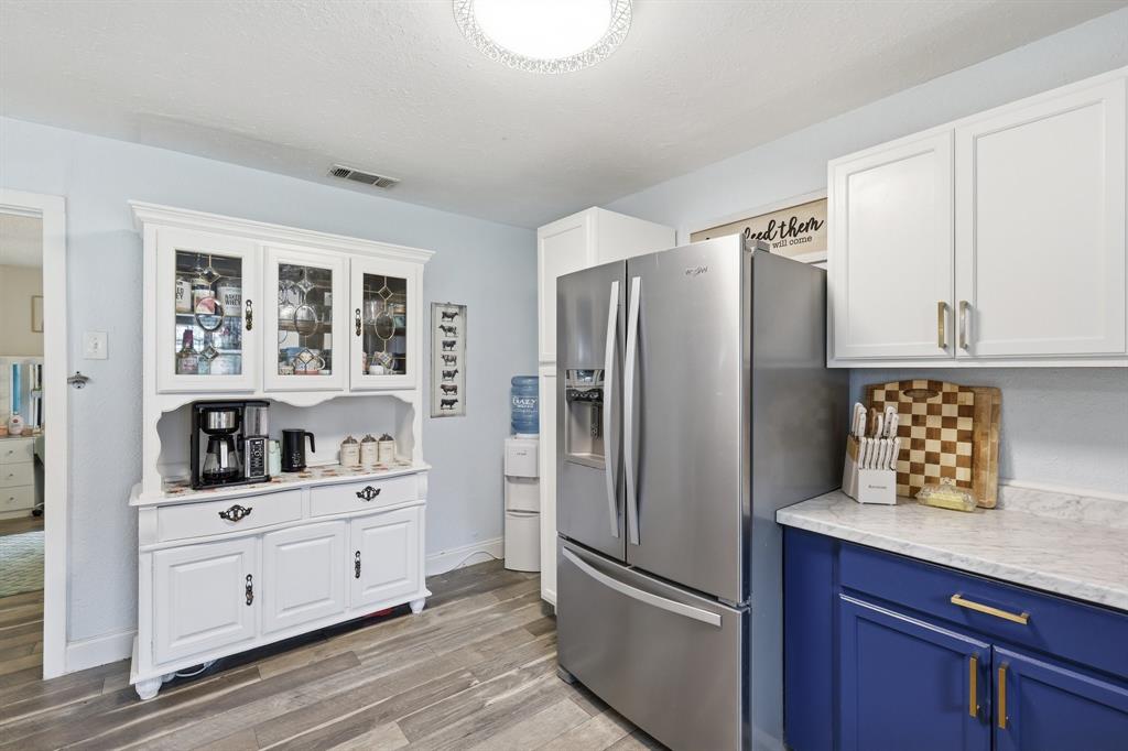 767 East Barry Street Azle, TX 76020 - Photo 33 of 40 The kitchen features a stainless steel refrigerator, white upper cabinets with gold-toned hardware, and contrasting blue lower cabinets