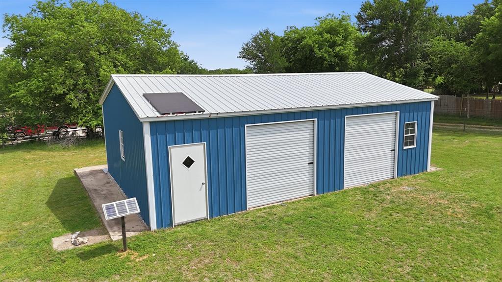 767 East Barry Street Azle, TX 76020 - Photo 4 of 40 The property includes a blue metal outbuilding with a white metal roof, featuring two garage doors and an entry door
