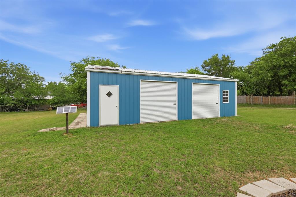767 East Barry Street Azle, TX 76020 - Photo 5 of 40 The property features a blue metal building with two garage doors and a white entry door, set on a concrete slab