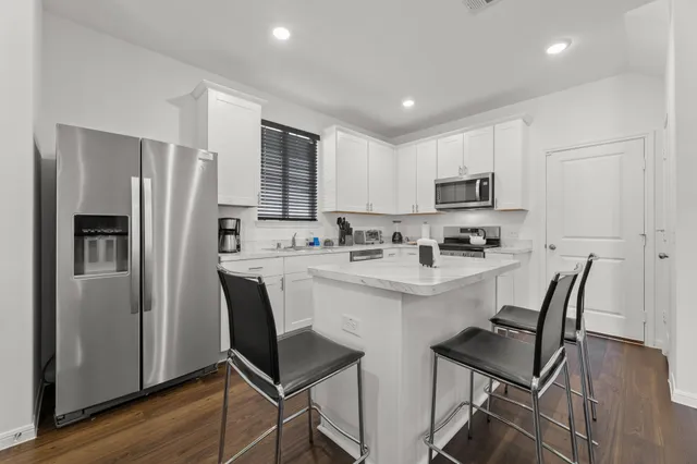 a kitchen with stainless steel appliances a refrigerator a stove a sink dishwasher a dining table and chairs with wooden floor