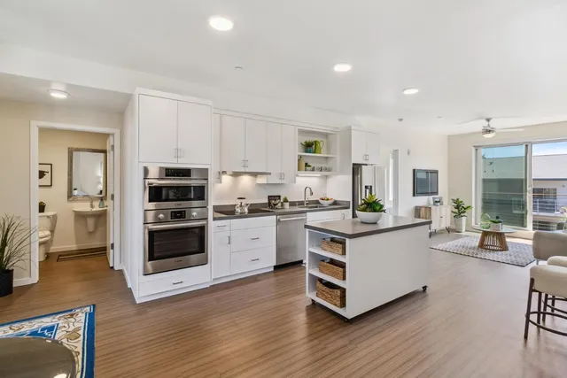 a kitchen with stainless steel appliances granite countertop a stove top oven a sink a refrigerator and white cabinets with wooden floor