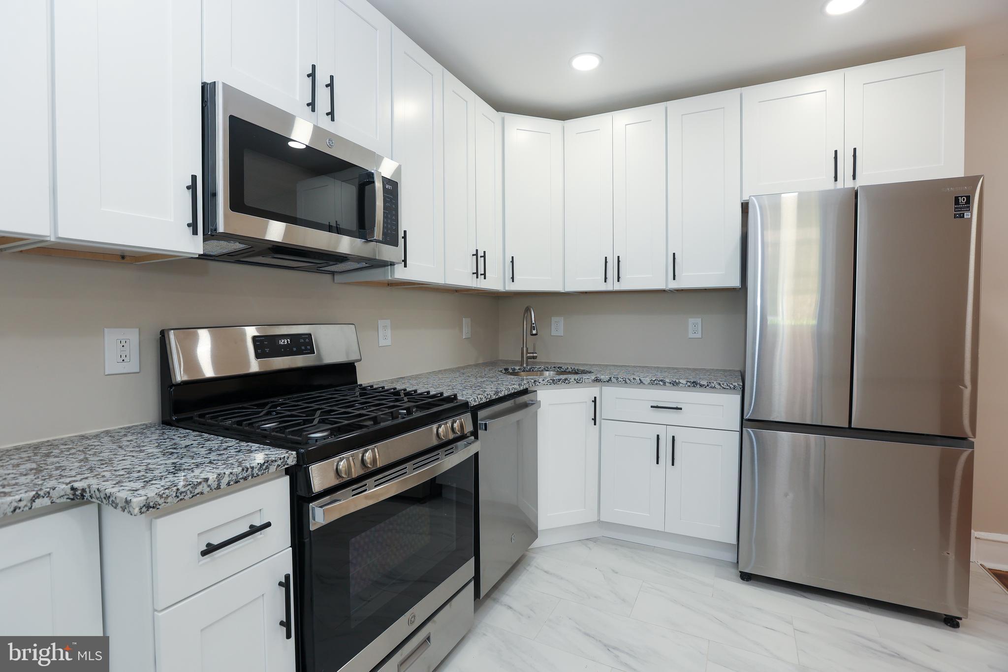 12 East Providence Road Lansdowne, PA 19050 - Photo 8 of 30 a kitchen with stainless steel appliances granite countertop a stove top oven a refrigerator and white cabinets