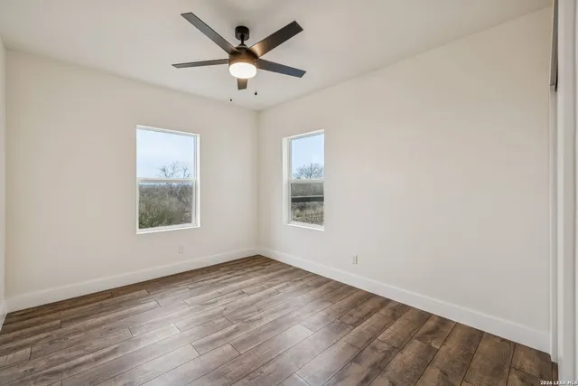 an empty room with a ceiling fan and kitchen view