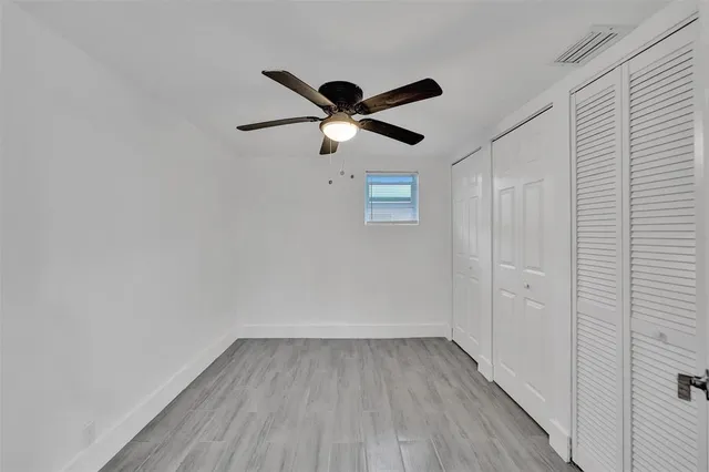 an empty room with wooden floor ceiling fan and window