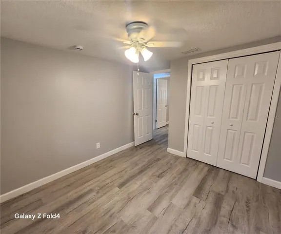 a view of an empty room with wooden floor and a ceiling fan