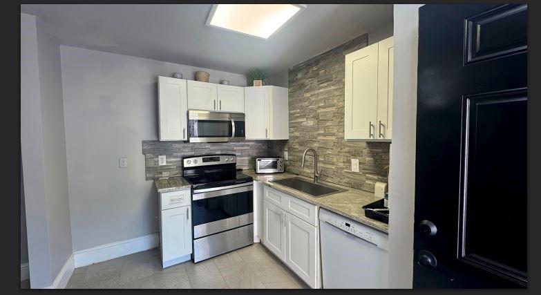 8110 Skillman Street, Unit 2057 Dallas, TX 75231 - Photo 4 of 16 Kitchen featuring tasteful backsplash, appliances with stainless steel finishes, white cabinets, and light stone counters