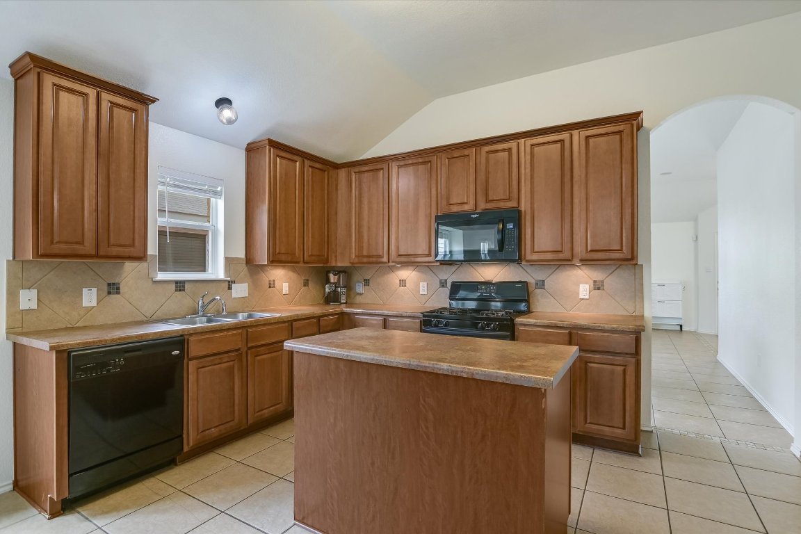 1901 Rachel Lane Round Rock, TX 78664 - Photo 19 of 35 Kitchen with a sink, arched walkways, light tile patterned flooring, vaulted ceiling, and black appliances