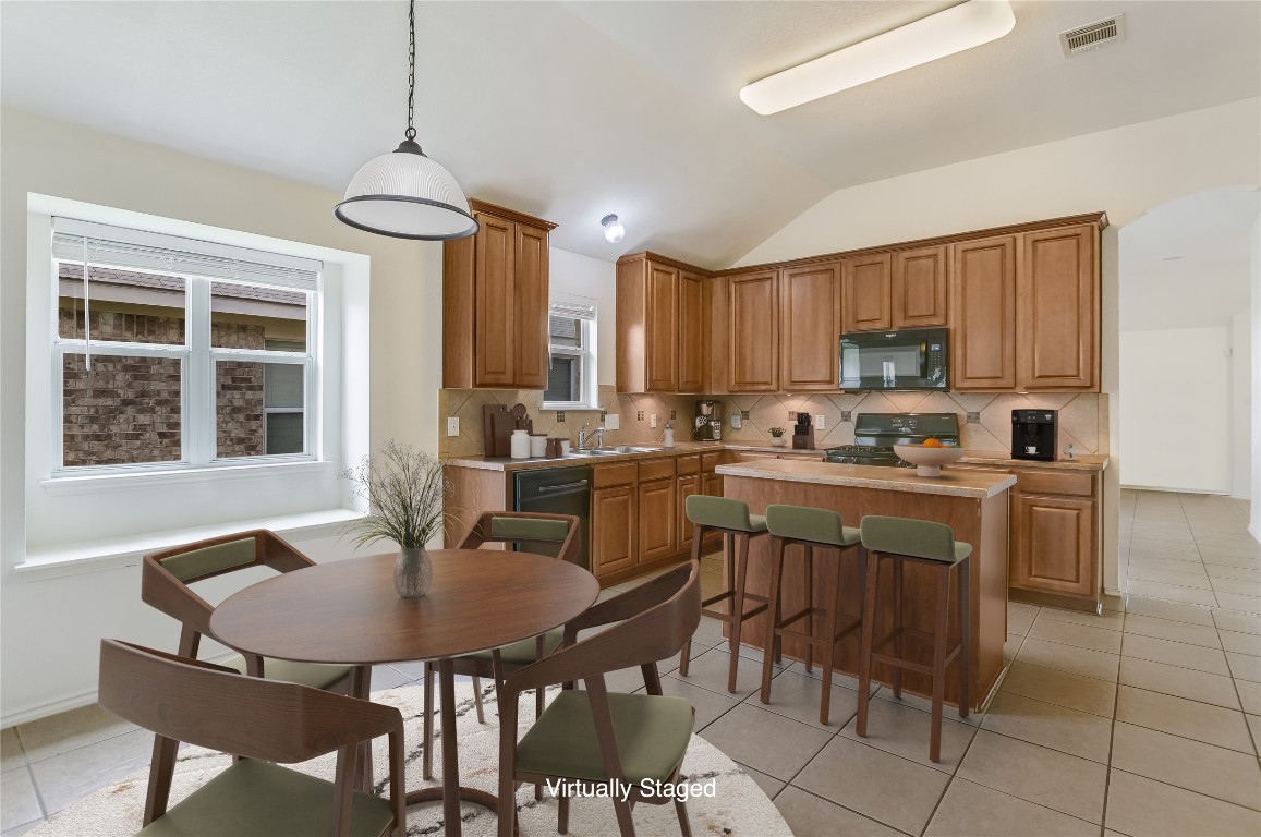 1901 Rachel Lane Round Rock, TX 78664 - Photo 22 of 35 Virtually Staged with Breakfast Room - Kitchen with black appliances, a center island, a sink, vaulted ceiling, and tasteful backsplash